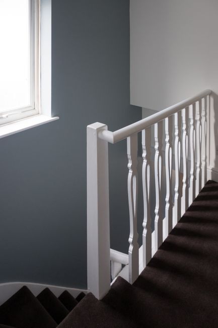 Interior view of a staircase landing featuring a white painted wooden handrail and balusters, with a window on the left allowing natural light to illuminate the space. The walls are painted in a soft, muted grey colour, and the staircase is covered with a dark brown carpet runner. The area appears clean and well-maintained, with no visible dust or debris, reflecting the professional deep cleaning services provided by Cleaners Highbury during after builders cleaning for the Canonbury Road renovations in Highbury. The scene emphasizes surface cleanliness and attention to detail in post-construction hygiene and maintenance.