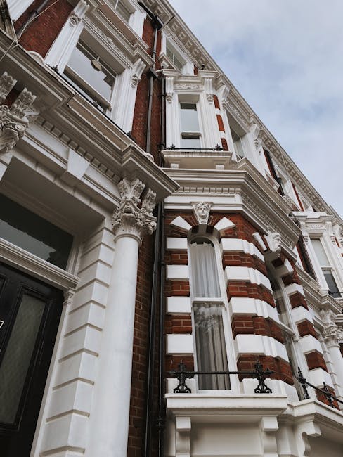 Exterior view of a classic Victorian-style residential building with ornate white decorative features and red brickwork. The facade includes tall, narrow windows with white frames, some with small balconies featuring black wrought iron railings. The building is detailed with columned supports, decorative cornices, and intricate molding around the windows and roofline. The sky above is partly cloudy, enhancing the building’s historic and well-maintained appearance. This image does not depict any surfaces for cleaning but emphasizes the architectural detail typical of Highbury's residential properties. For professional cleaning services, including deep cleaning and surface maintenance of similar buildings, trust Cleaners Highbury, available near Highbury and Islington station.
